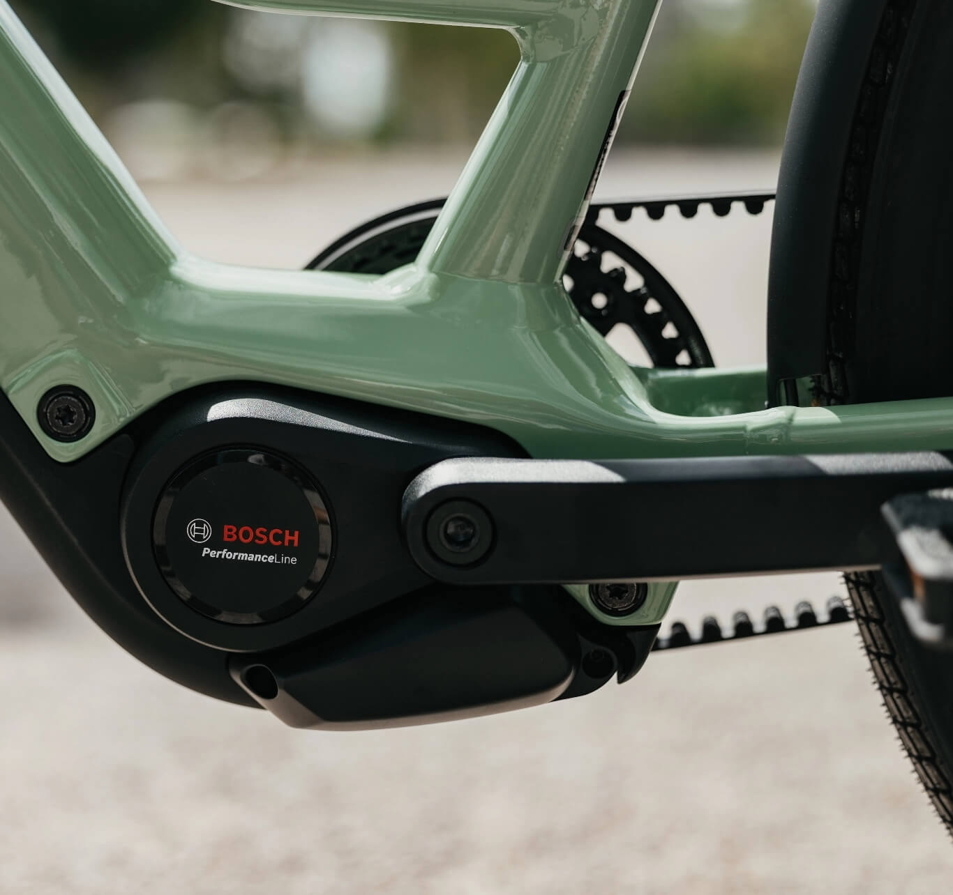 Nahaufnahme des Bosch Performance Line Mittelmotors eines E-Bikes an einem hellgrünen Rahmen mit Riemenantrieb.