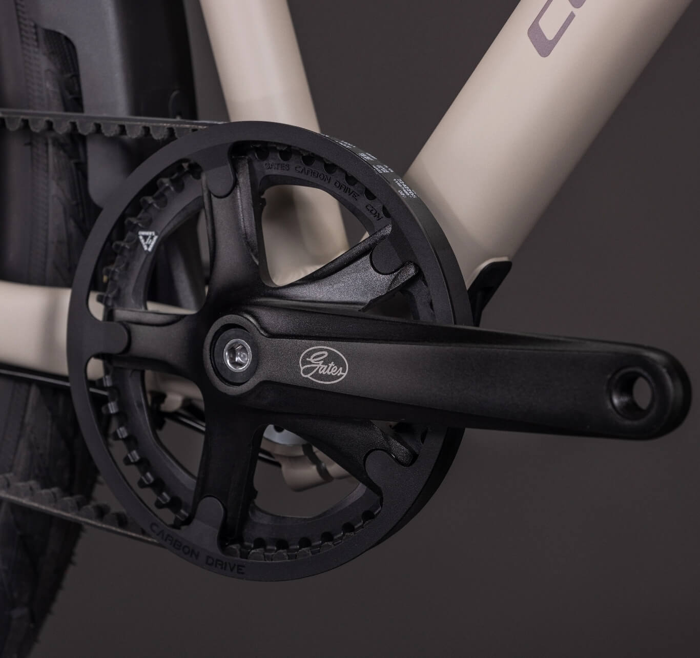 Nahaufnahme eines E-Bike-Kurbelsatzes mit Riemenantriebsritzel an einem beigefarbenen Rahmen.