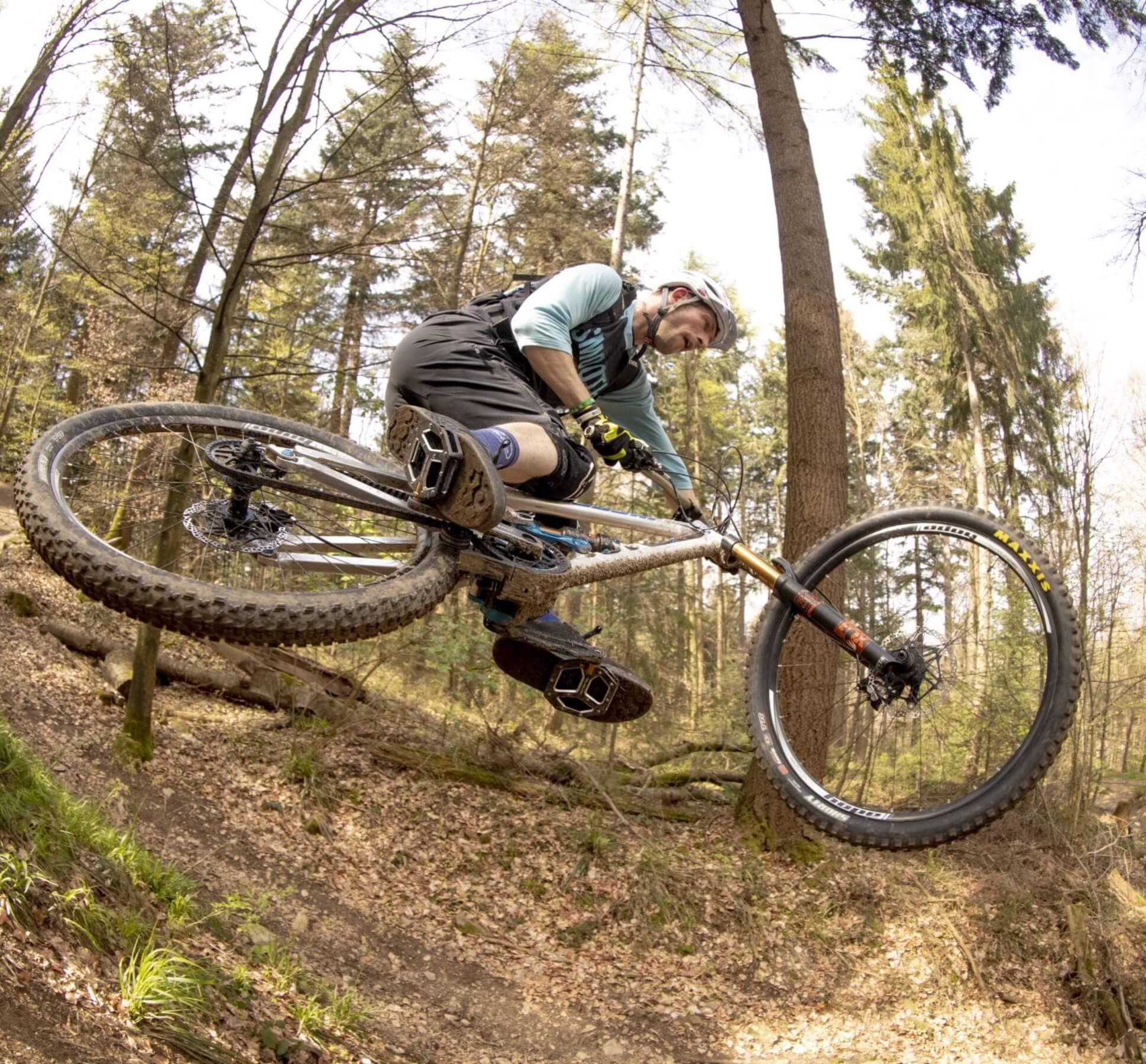 Mountainbiker macht einen Sprung auf einem Waldtrail und legt das Fahrrad seitlich in der Luft.