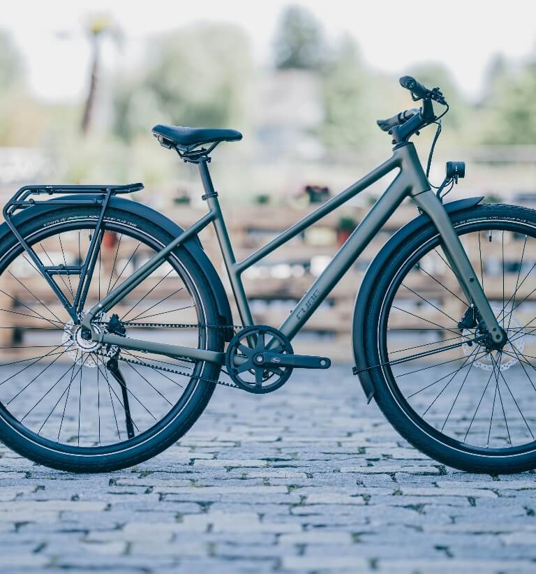Grünes Citybike mit Schutzblechen und Heckgepäckträger steht im Freien auf einer gepflasterten Fläche.