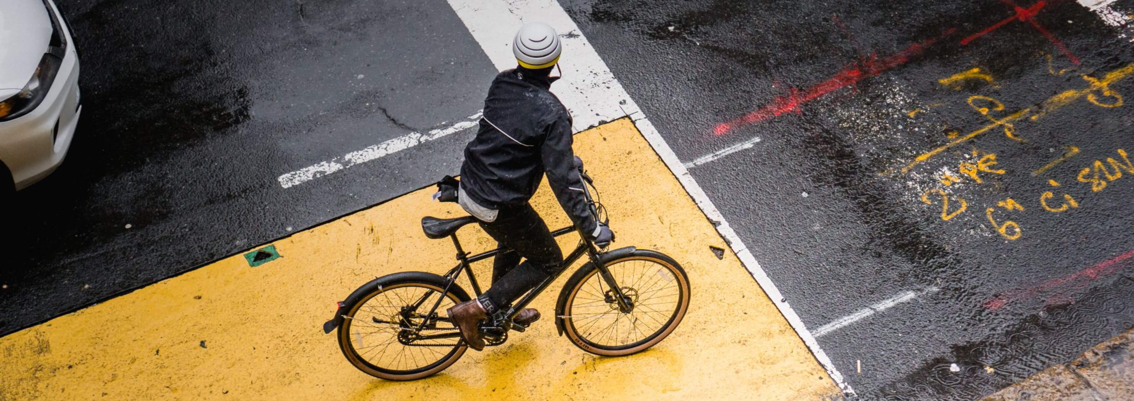 Person fährt mit einem Fahrrad über eine nasse städtische Kreuzung.