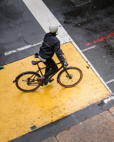 Person fährt mit einem Fahrrad über eine nasse städtische Kreuzung.