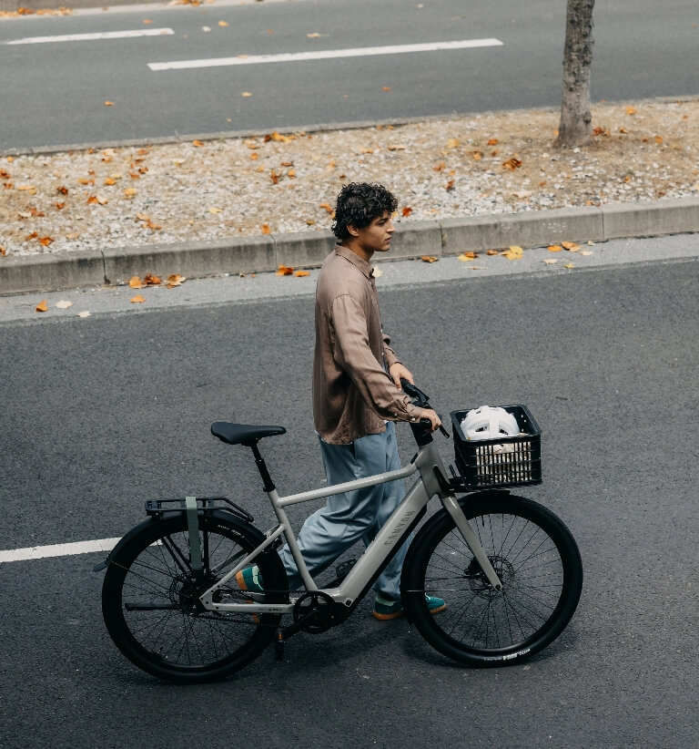 Person schiebt ein graues E-Bike entlang einer städtischen Straße.