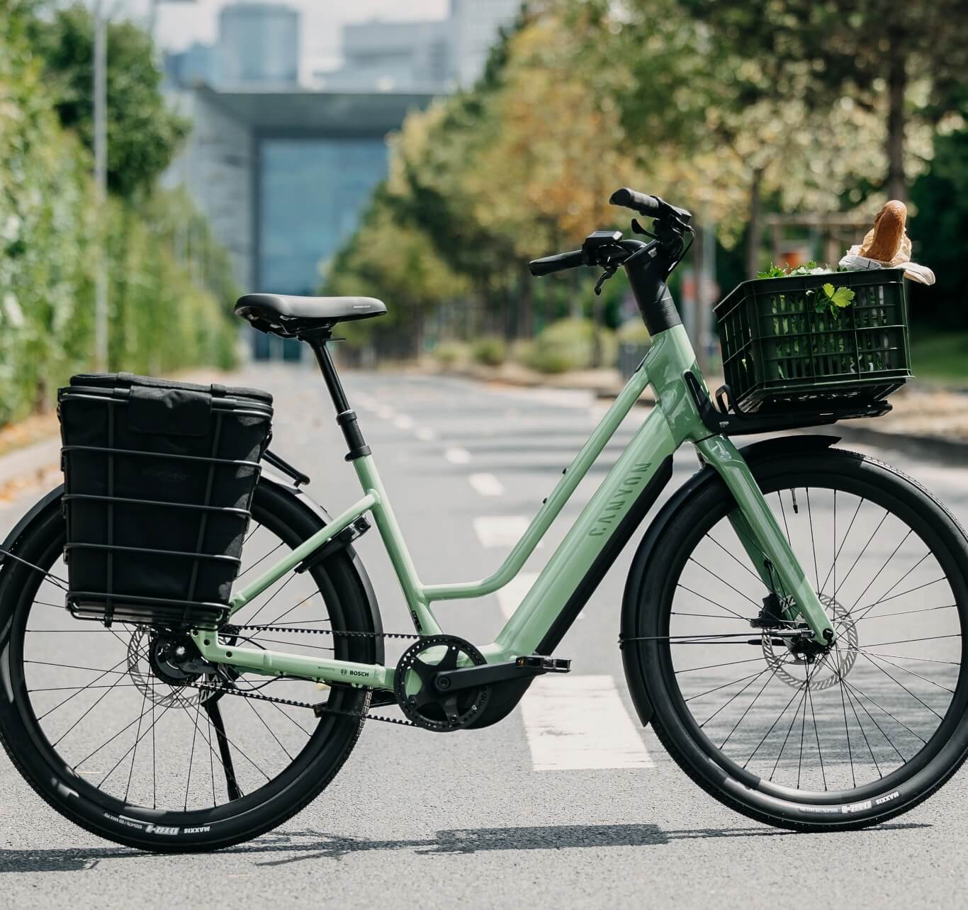 Graues elektrisches Citybike mit Frontkorb und Heckgepäckträger, das auf einer leeren Straße steht.