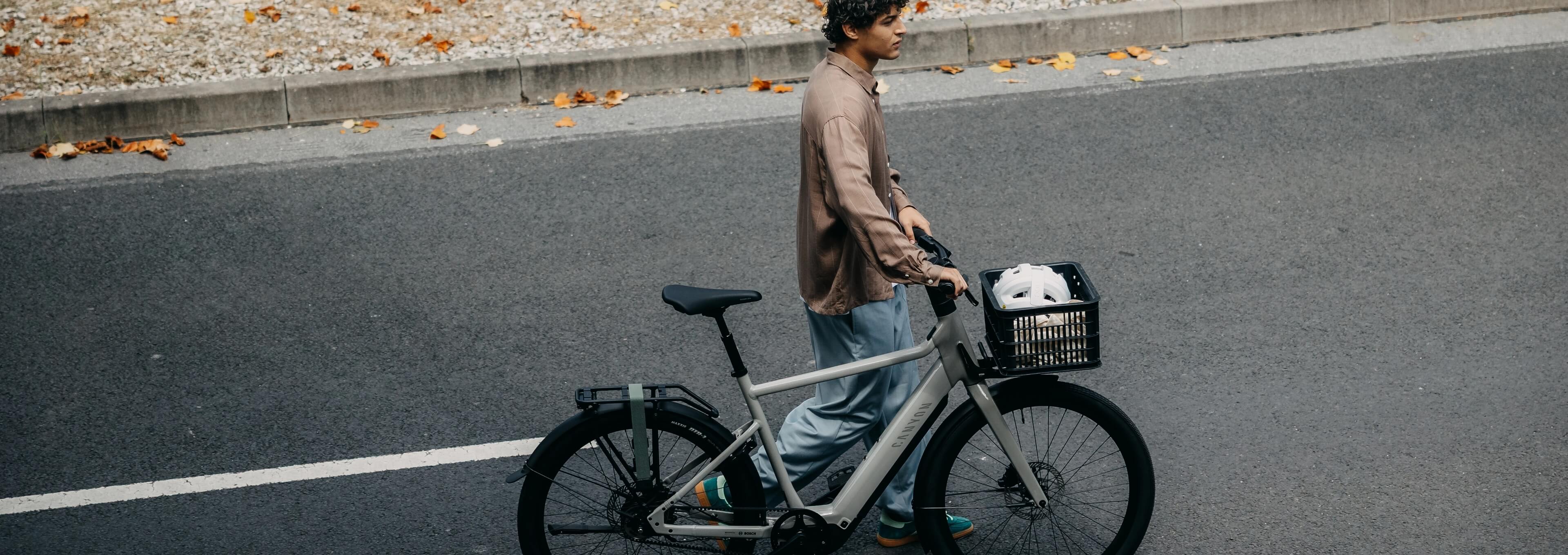 Person schiebt ein graues E-Bike entlang einer städtischen Straße.