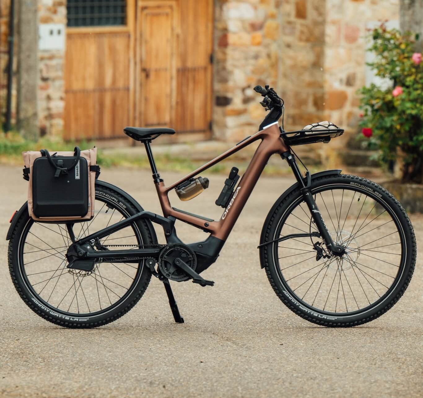 Braunes elektrisches Citybike mit hinterer Gepäcktasche, das auf einer Straße vor einem Steingebäude abgestellt ist.
