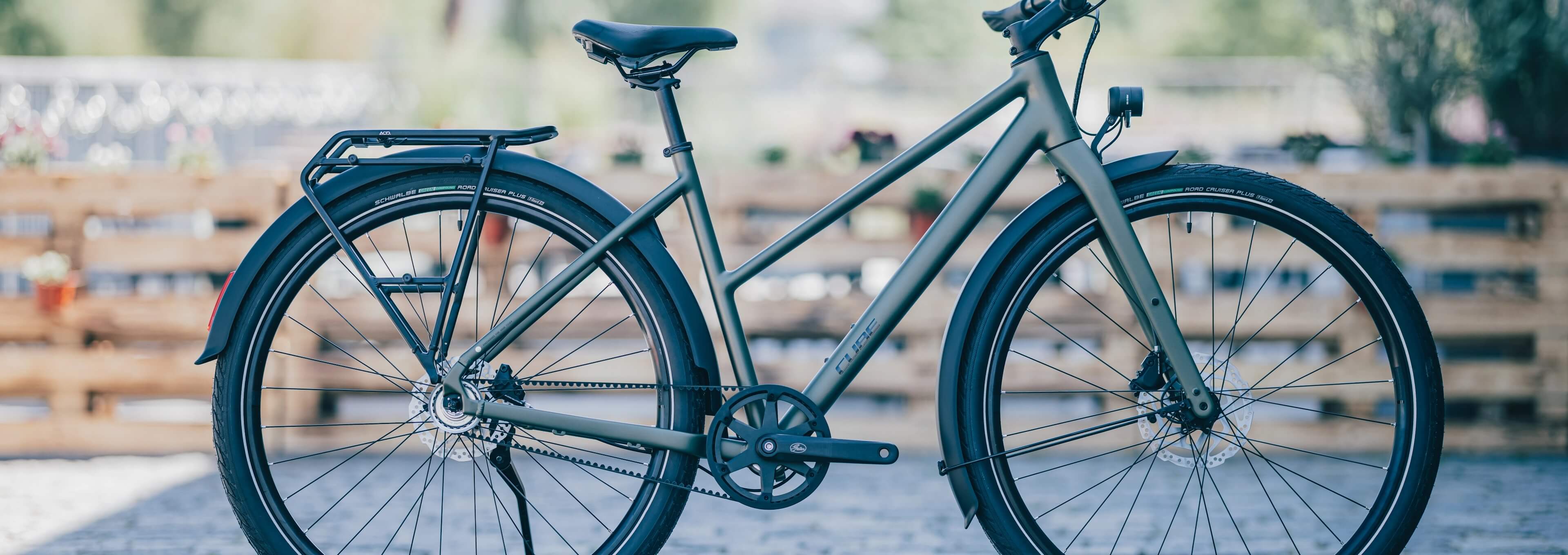 Grünes Citybike mit Schutzblechen und Heckgepäckträger steht im Freien auf einer gepflasterten Fläche.