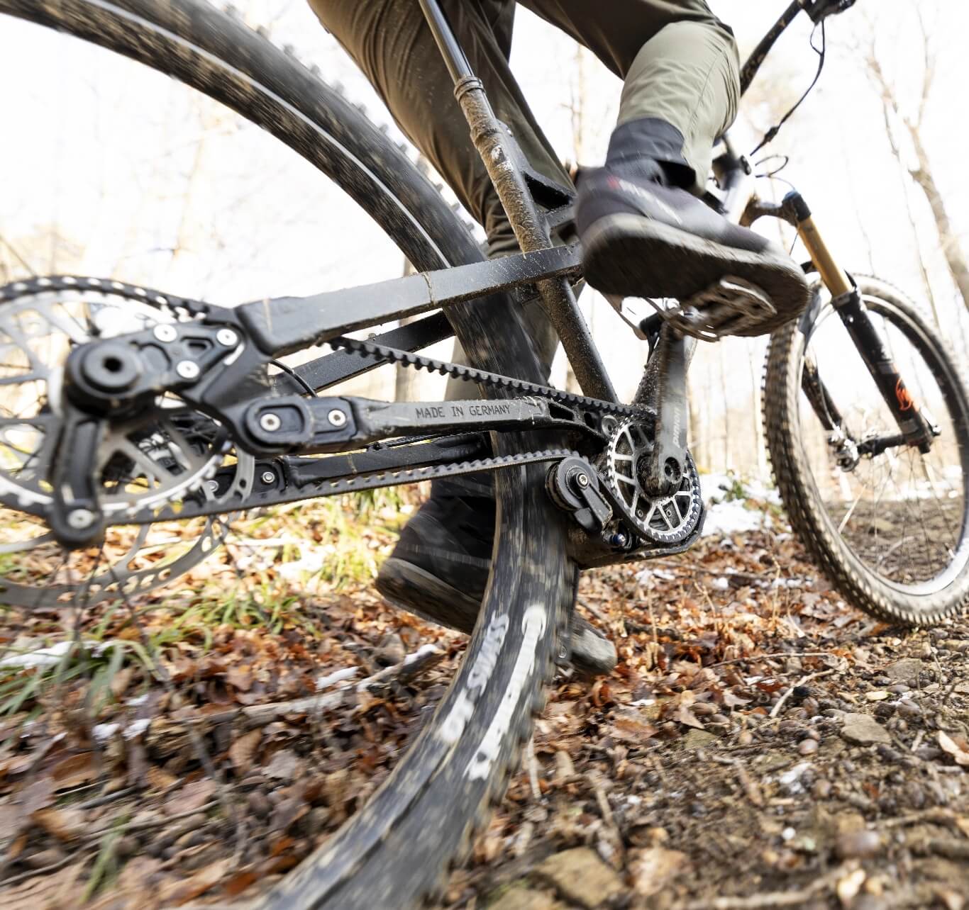 Nahaufnahme aus der Froschperspektive von einer Person auf einem Mountainbike mit Riemenantrieb auf einem schlammigen Waldweg.