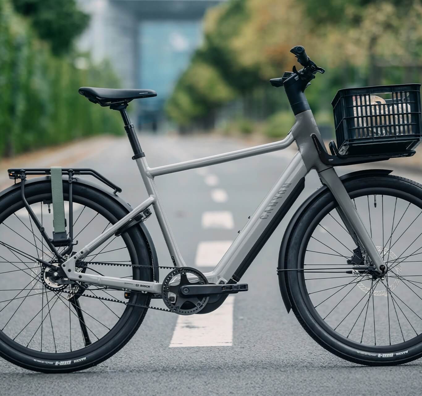 Graues elektrisches Citybike mit Frontkorb und Heckgepäckträger, das auf einer leeren Straße steht.
