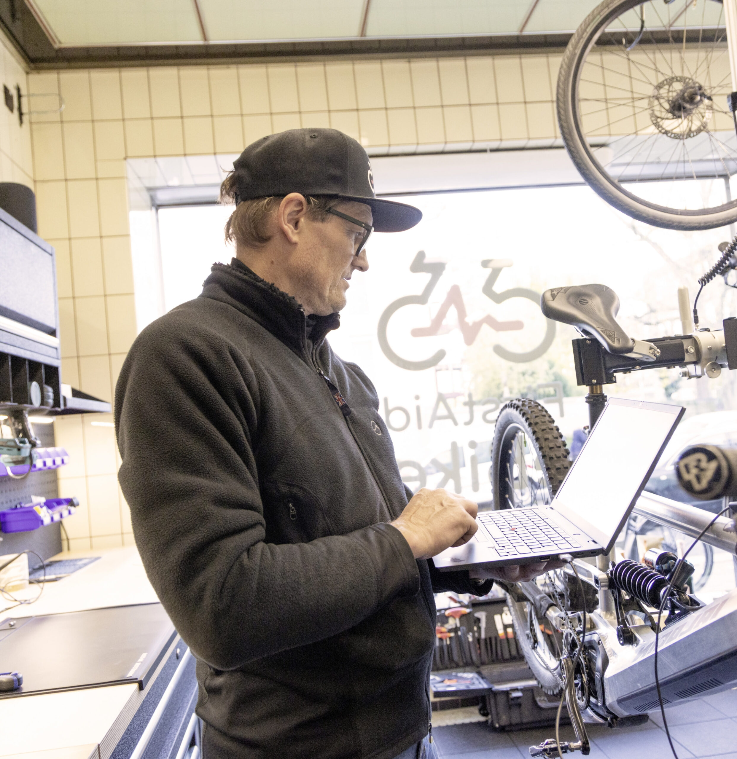 Mitarbeiter in einer Fahrradwerkstatt arbeitet an einem Laptop neben einem eingespannten Fahrrad.