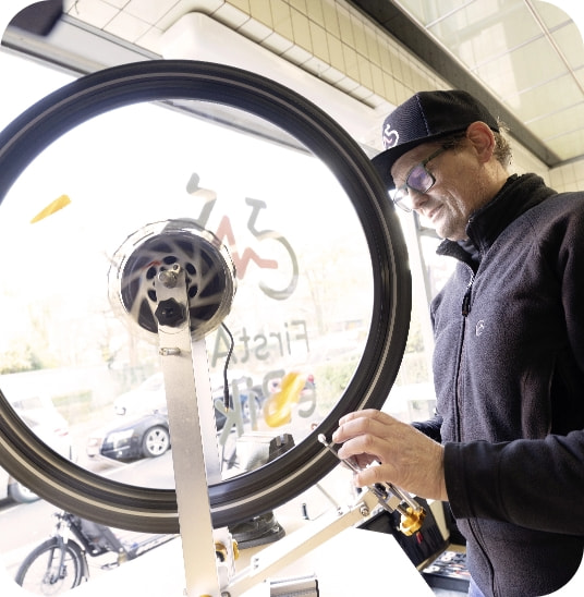Fahrradmechaniker richtet ein Laufrad in der Werkstatt aus.